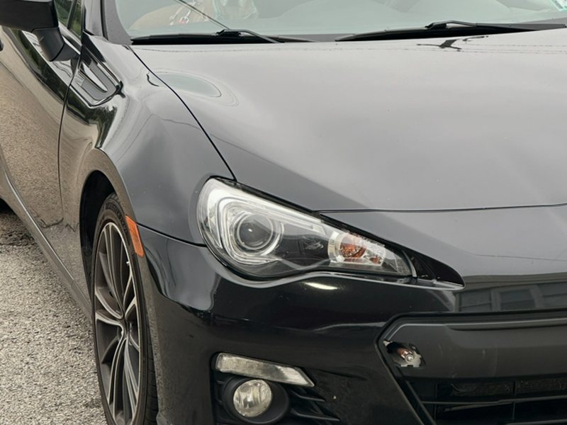 Close phone photo of the black coupe's headlight, front bumper and fog light