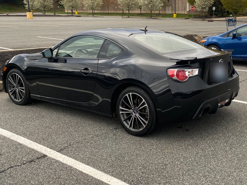 Phone photo of the black coupe from the rear, driver's side, with its plate blurred