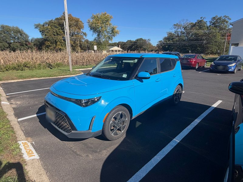 Phone photo of a blue crossover in a parking lot, seen from the front driver's side, plate blurred